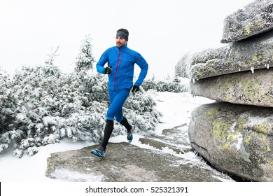 young man in blue sportswear running on the snow frozen trail in winter mountains with cold fog