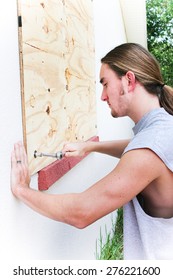 Young Man Boarding Up Windows To Prepare For Natural Disaster Such As Hurricane Or Tornado.  