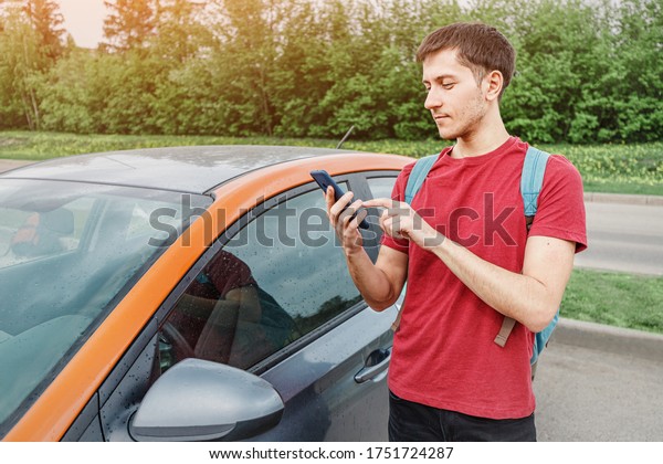 young man books a car or taxi on a\
smartphone in the carsharing app to get around the city. New\
generation chooses not to own a car but to rent a\
vehicle