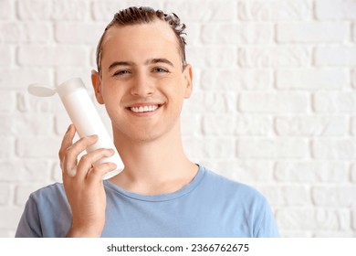Young man with bottle of shampoo on white brick background - Shutterstock ID 2366762675