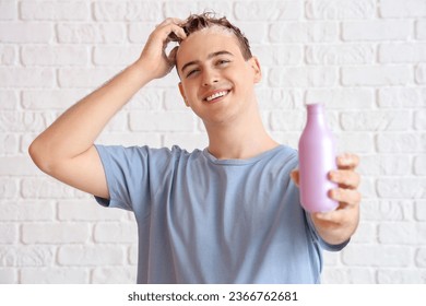 Young man with bottle of shampoo on white brick background - Shutterstock ID 2366762681