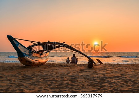 Young man and boy, father and son, dog sitting on the beach at sunset, Kalutara, Sri Lanka