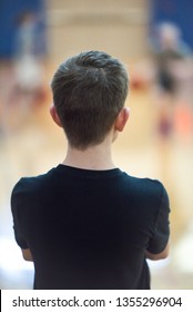 A Young Man Or Boy Waits Patiently On The Sidelines As He Watches His Team During A Basketball Game For His Turn To Play.