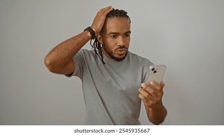 Young man with braids looks surprised at smartphone over white background, showing expression of disbelief, wearing gray t-shirt, isolated indoors, african american male. - Powered by Shutterstock