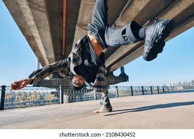 Young man break dancer dancing on urban background performing acrobatic stunts. Street artist breakdancing outdoors