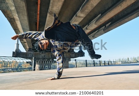 Young man break dancer dancing on urban background performing acrobatic stunts. Street artist breakdancing outdoors