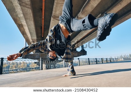 Young man break dancer dancing on urban background performing acrobatic stunts. Street artist breakdancing outdoors