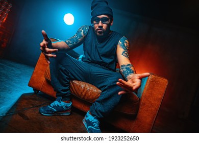 Young man break dancer sitting in big old chair portrait. Tattoo on hands. - Shutterstock ID 1923252650