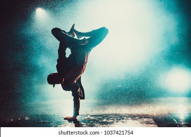 Young man break dancing in club with lights and water. Blue dramatic colors.