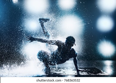 Young man break dancing in club with lights and water. Tattoo on body. Blue tint colors.