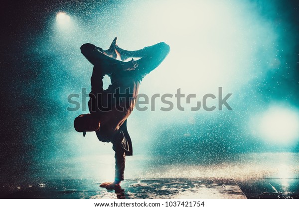 Young man break dancing in club with lights and\
water. Blue dramatic\
colors.
