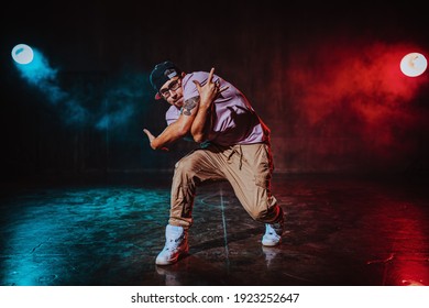 Young man break dancing in dark hall with blue and red lights. Tattoo on hand. - Shutterstock ID 1923252647
