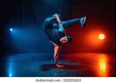 Young man break dancing in dark hall with blue and red lights. Tattoo on hands. - Shutterstock ID 1923252653