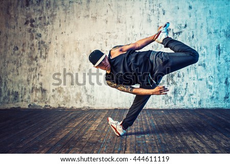 Young man break dancing on wall background. Tattoo on body.
