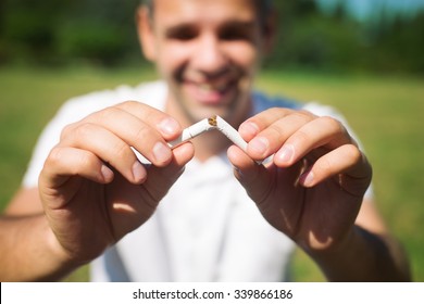 Young Man Is Breaking A Cigarette On Green Background, Quit Smoking Concept