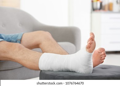 Young Man With Broken Leg In Cast Sitting On Sofa At Home