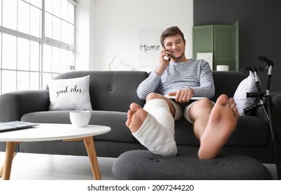 Young Man With Broken Leg Talking By Phone At Home