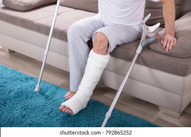 Young Man With Broken Leg Using Crutches To Get Up From Sofa