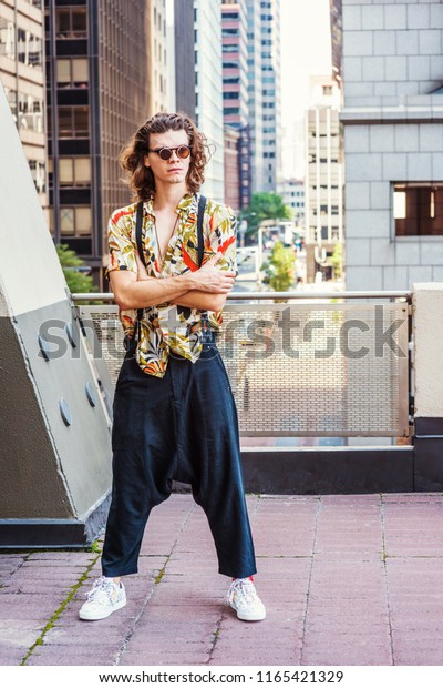 Young Man with brown curly hair, wearing\
sunglasses, patterned short sleeve shirt, baggy loose pants with\
suspenders, patterned sneakers, hanging old key as necklace,\
standing on balcony in New\
York.\
