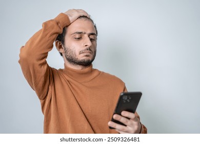 A young man in a brown sweater looking stressed and confused while checking his smartphone, perfect for illustrating frustration or worry related to modern communication or technology. - Powered by Shutterstock