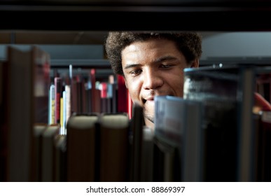 Young Man Browsing Through The Racks Of Books In A Library