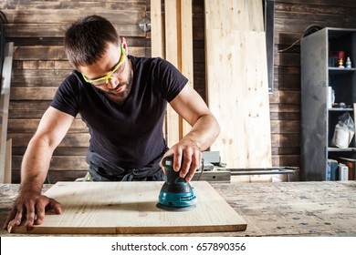 Young man builder carpenter equals polishes wooden board with a  random orbit sander  in the workshop - Powered by Shutterstock