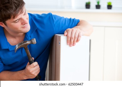 Young Man Building Furniture Using A Hammer And A Nail At Home