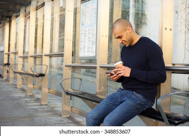 young man at the bus stop with a coffee and phone
