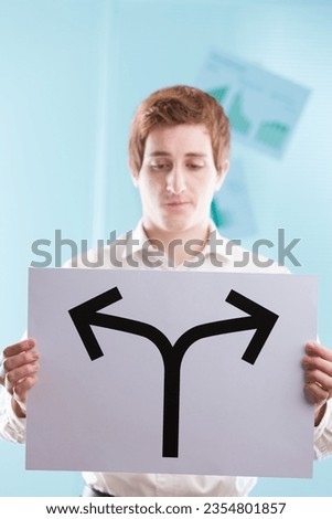 Young man, business backdrop, presents an arrow-sign stopping at a bifurcation. It's a stark reminder: every step forward or backward is an intentional choice