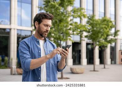 A young man businessman, freelancer stands near an office building and uses a mobile phone. - Powered by Shutterstock