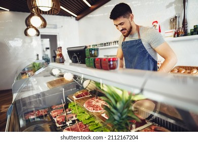 Young Man Butcher Arranging Meat Products In Display Case Of Butcher Shop