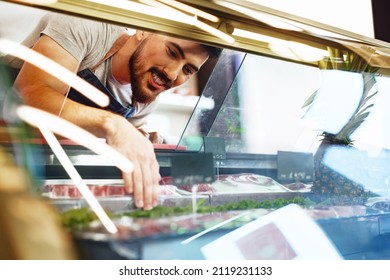 Young Man Butcher Arranging Meat Products In Display Case Of Butcher Shop