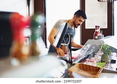 Young Man Butcher Arranging Meat Products In Display Case Of Butcher Shop