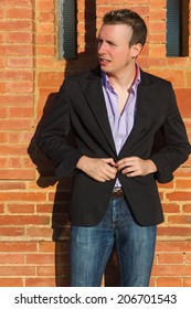 Young man buttoning his jacket in the sun in front of a brick wall 