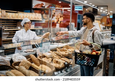 Young man buying bread in supermarket bakery. Focus is on female baker.  - Powered by Shutterstock