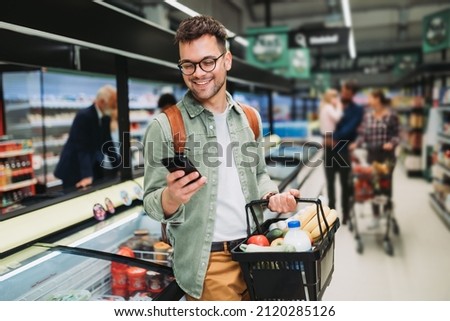 Young man buying groceries at the supermarket. Other customers in background. Consumerism concept.