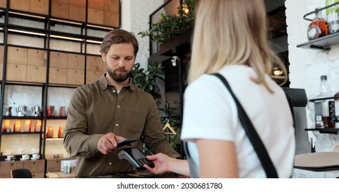 Young Man Is Buying Takeaway Coffe In Coffee-shop And Paying With Smartphone Making Contactless Payment. Modern Technology And Banking Concept.