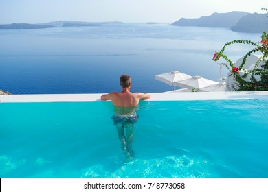 Young Man By The Swimming Pool At A Luxury Resort By The White Traditional Houses At The Village Of Oia Santorini Greece