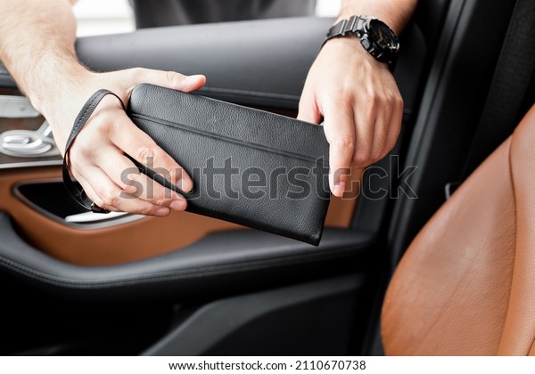 A young man in the cabin of a luxury car\
holds a black leather wallet in his\
hands.