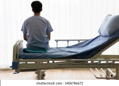 A young man cancer patient sitting alone on a hospital bed is distraught looks out the window with sick sad thoughtfulness. Chemotherapy and convalescence in recuperation release suffering from ill. - Powered by Shutterstock