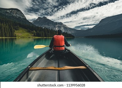Young Man Canoeing on Emerald Lake in the rocky mountains canada with canoe and life vest with mountains in the background blue water. - Powered by Shutterstock