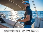 Young man captain stands at the helm and controls a sailboat during a journey by sea. High quality photo