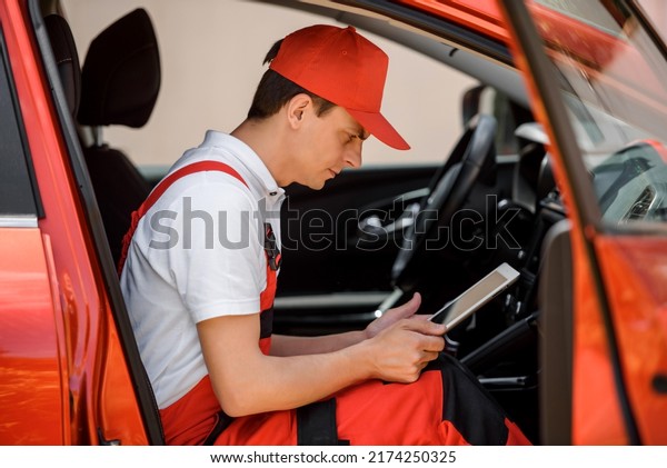 Young\
man car electrician mechanic is using a tablet computer to check\
the car battery errors and problems and fix it.\
\
