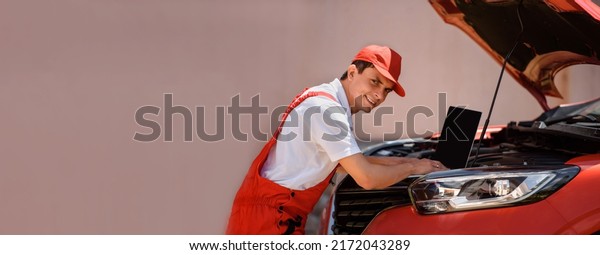 Young man car mechanic electrician is using an laptop\
computer to check diagnostic the car errors and problems and fix\
it. \
