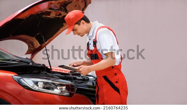 Young man car mechanic is using a tablet computer\
to check the car errors and problems and fix it.  Copy space for\
your text\
