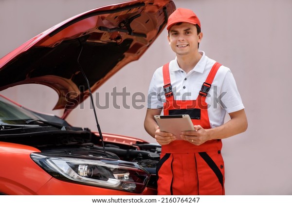 Young man car mechanic is
using a tablet computer to check the car errors and problems and
fix it. 
