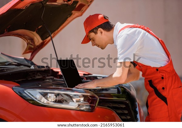 Young man car
mechanic is using an laptop computer to check diagnostic the car
errors and problems and fix it.

