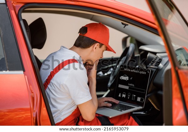 Young man car mechanic is using an laptop\
computer to check diagnostic the car errors and problems and update\
the car software.\
