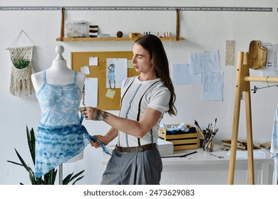 A young man carefully adjusts a blue tie-dye garment on a dress form in his clothing restoration atelier. - Powered by Shutterstock