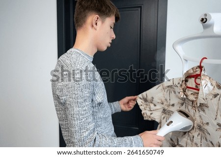 A young man is carefully steaming a patterned shirt to remove wrinkles, embodying the essence of preparation for a stylish event in a contemporary indoor setting.